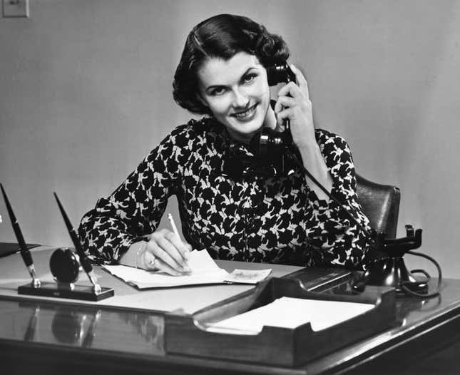 Businesswoman is shown speaking on telephone at a desk.