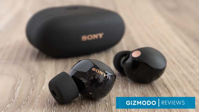 A close-up of an in-focus Sony WF-1000XM5 wireless earbud with the other earbud, and the charging case, appearing slightly out of focus in the background.
