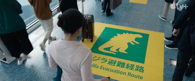 Una mujer mira fijamente un cartel que dice “Ruta de evacuación de Godzilla”