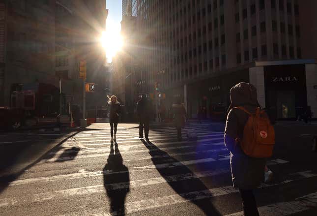 People walk across Broadway in lower Manhattan as the sun rises on January 24, 2023, in New York City. 