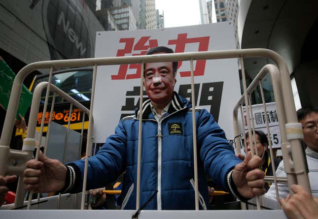 A protester wearing a mask of missing bookseller Lee Bo sits in a cage.