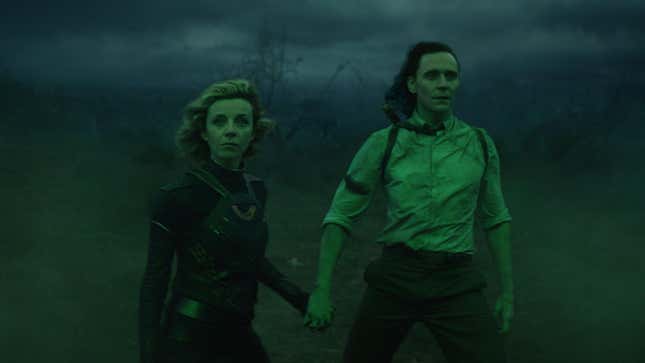  Loki (Tom Hiddleston) and Sylvie (Sophia Di Martino) are bathed in green while holding hands.