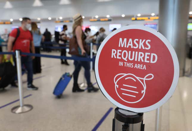A sign reading, ‘masks required in this area,’ is seen as travelers prepare to check-in for their Delta Airlines flight at the Miami International Airport.
