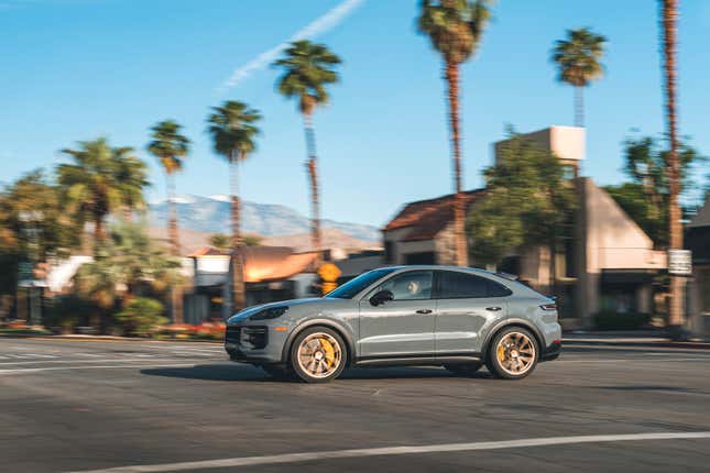 The 2024 Porsche Cayenne GT drives through a city intersection. There are palm trees in the background.