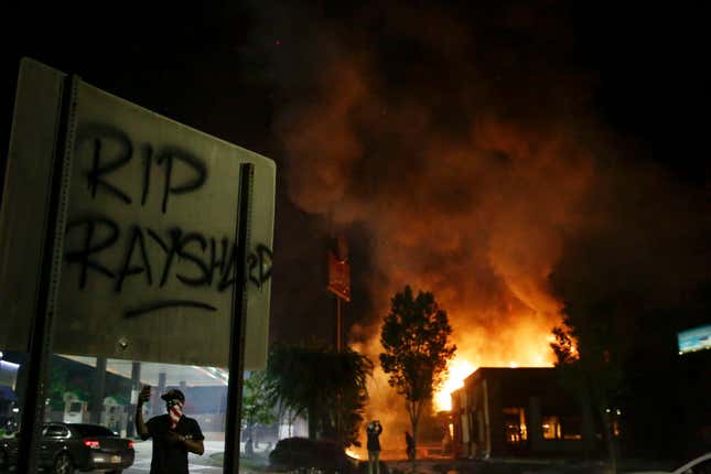 In this Saturday, June 13, 2020, file photo, “RIP Rayshard,” is spray-painted on a street sign as flames engulf a Wendy’s restaurant during protests in Atlanta. The restaurant was where Rayshard Brooks was shot and killed by police the previous evening following a struggle in the drive-thru line.