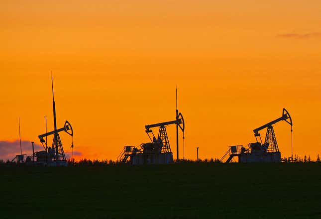 Three oil rigs in silhouette against an orange sky.