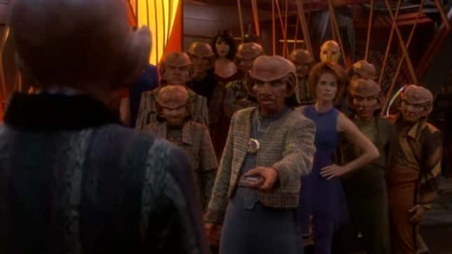 Rom hands his brother Quark a padd filled with union demands, as Leeta and the other bar workers look on behind him.