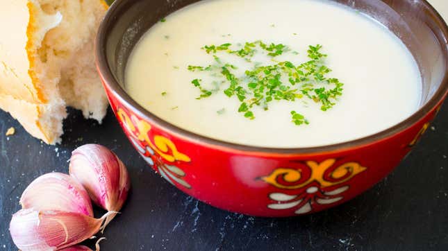Bowl of ajo blanco soup beside garlic cloves and bread