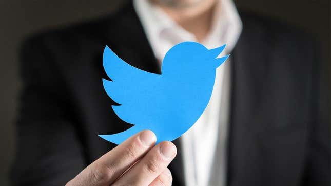 A man in a suit holds up the Twitter logo