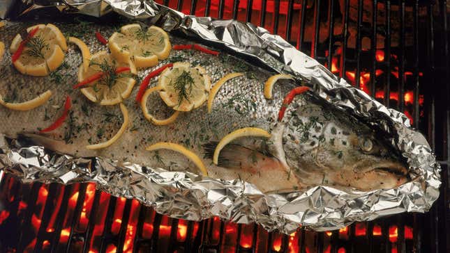 Grilled fish with lemon slices sitting on foil over charcoal grill