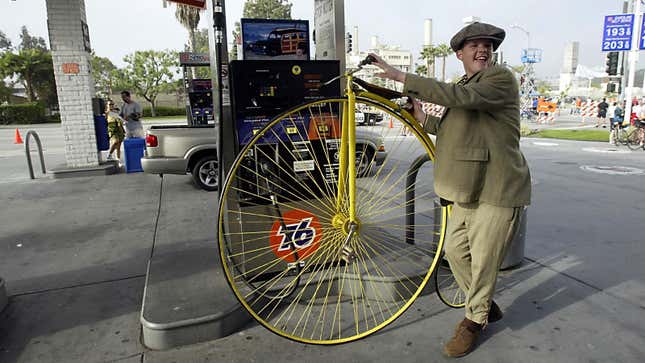 A photo of a man riding an old fashioned bike through a gas station.