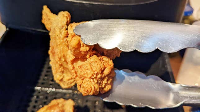fried chicken wing held by tongs