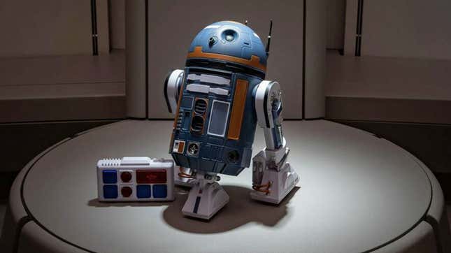 A blue and orange droid sits on a pedestal, part of the scene at Galactic Starcruiser.