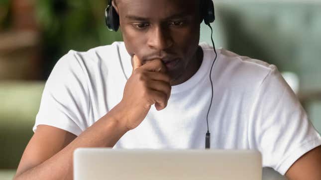 An African American man studies the screen of his laptop intently while wearing headphones