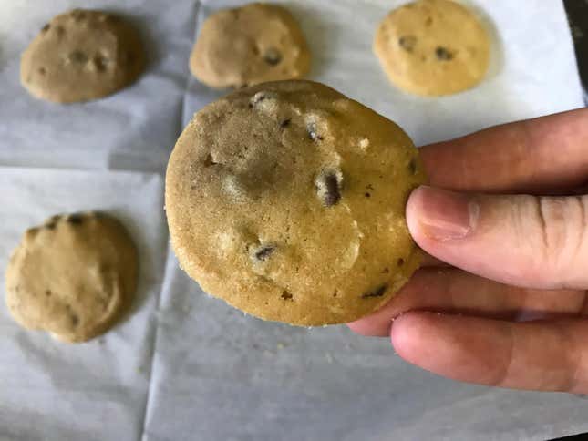 A hand holding a cookie above four other cookie on a baking tray.
