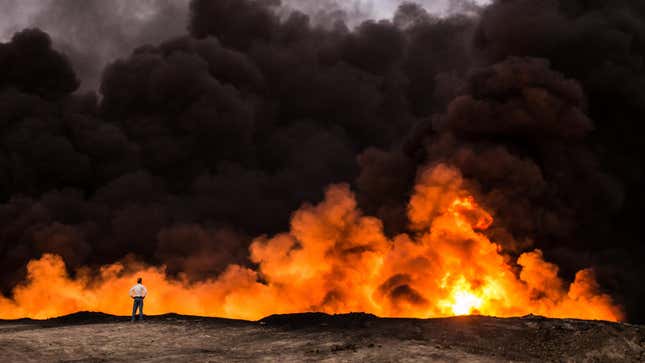 A man stands in front of a fire from oil that has been set ablaze in Iraq. 