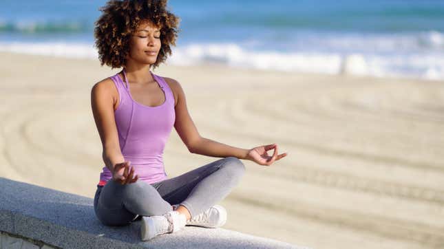 a Black woman meditates on the beach, sitting in the lotus position