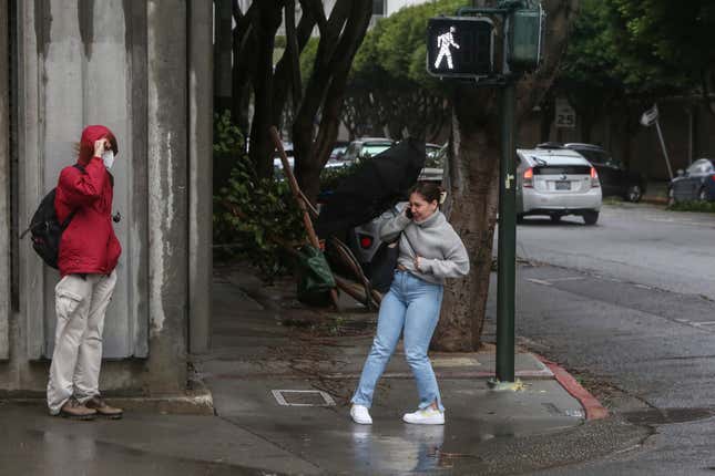 A pedestrian struggles with her umbrella in high winds and rain on Davis Street in the Embarcardero in San Francisco California, on Tuesday, March 21, 2023.