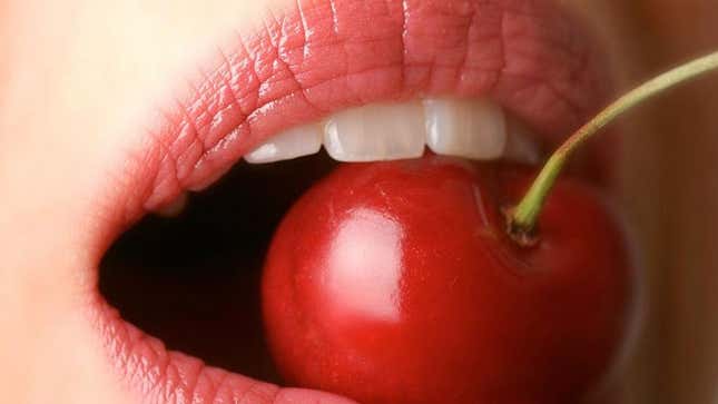 Close-up of woman's mouth biting into bright red cherry