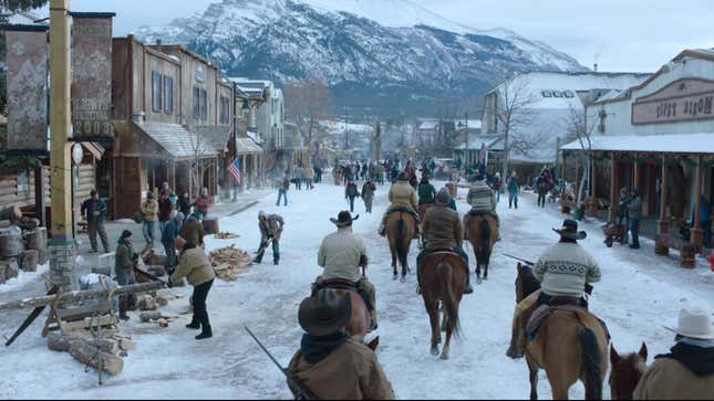 Joel and other people are seen on horseback riding down a wide, snowy street in a bustling town in a scene from HBO's The Last of Us.