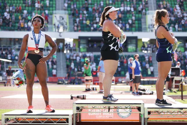Gwendolyn Berry, left, third place, looks on during the playing of the national anthem with DeAnna Price, center, first place, and Brooke Andersen, second place, on the podium after the Women’s Hammer Throw final on day nine of the 2020 U.S. Olympic Track &amp; Field Team Trials at Hayward Field on June 26, 2021 in Eugene, Oregon.