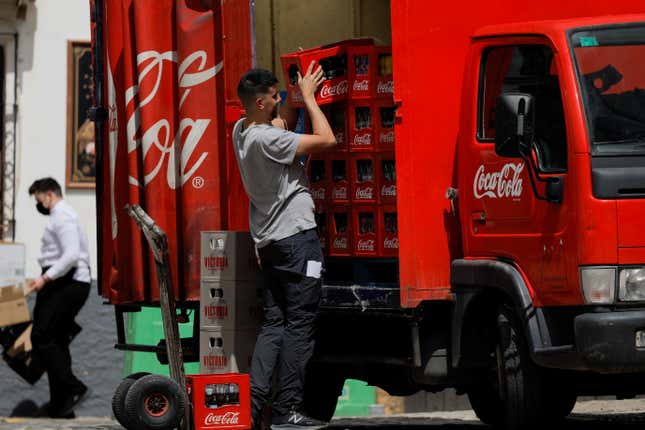 A man unloads a stacked case of Coca-Cola from a bright red Coca-Cola truck.