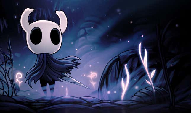 Main character in Hollow Knight, a creature with a white face, horns, big black eyes, and a tattered gray cape, standing on cobblestones near dark vegetation in a promotional image.