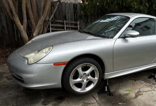 A silver 2003 Porsche 911 is on jacks, displaying its front wheel.