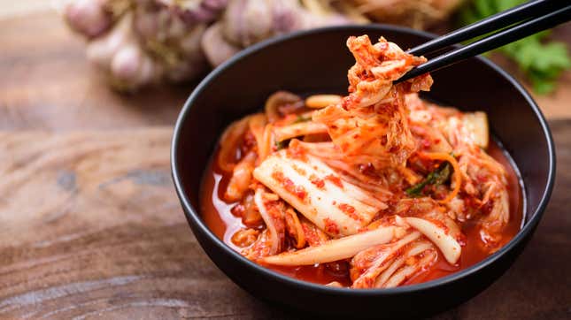A chopstick picks up a piece of cabbage from a brightly colored bowl of kimchi 