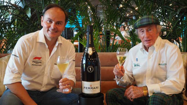 Ferrari Trento CEO Mario Lunelli sits next to former F1 Champion Jackie Stewart, with a bottle of Ferrari Trento sparkling wine between them.