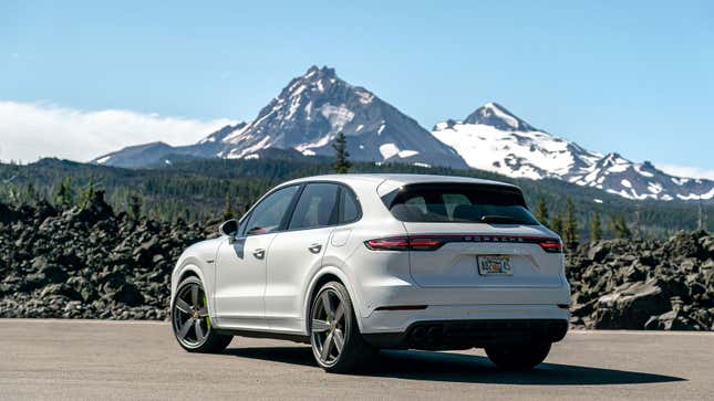 A white Porsche Cayenne SUV parked in front of a mountain. 