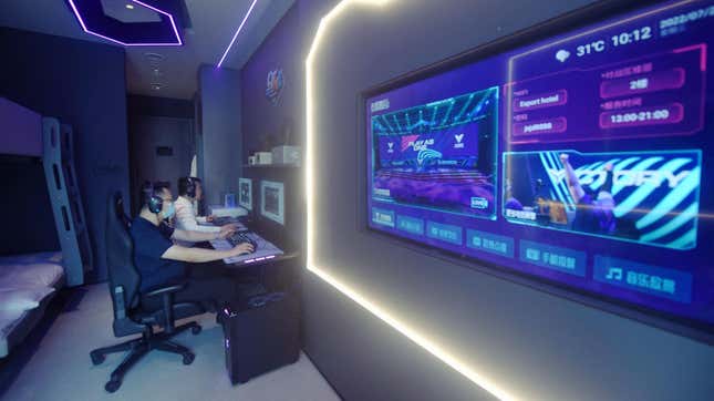 Two young people play video games at computers under low lights and neon 