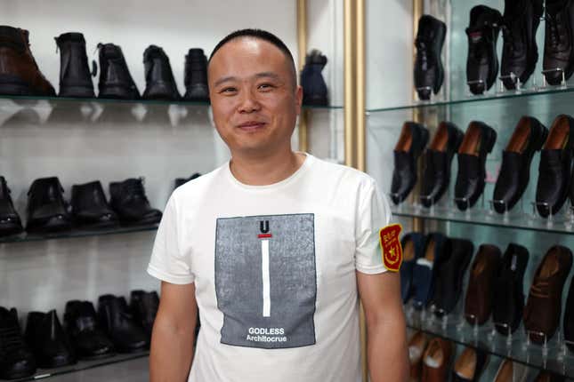 Xiaopeng Gao stands in front of a shelf of men's shoes at his store in Khorgos ICBC. He wears the badge that says "security personnel."