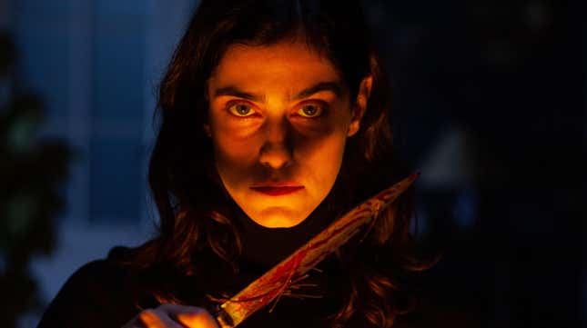 A woman, in shadow except for light across her face, holds a bloody knife in a scene from The Advent Calendar.