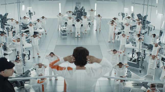 Cassian looks out into a sterile white room where prisoners make widgets.