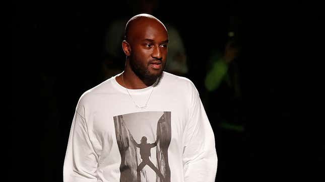 This is an image of Virgil Abloh from head to waist. He is wearing a white shirt with a man pushing against walls. He also has a silver chain on.