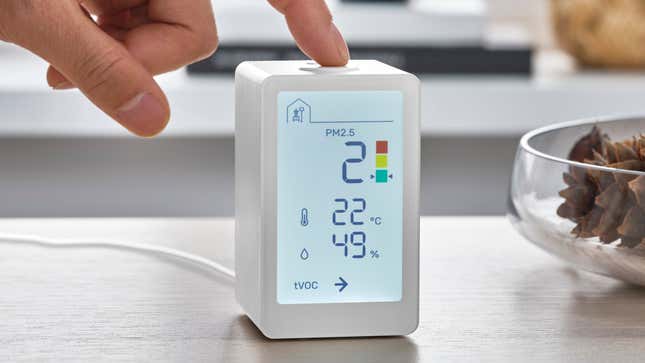 A user pressing a button atop the Ikea Vindstyrka indoor air quality monitor, sitting on a wooden table.