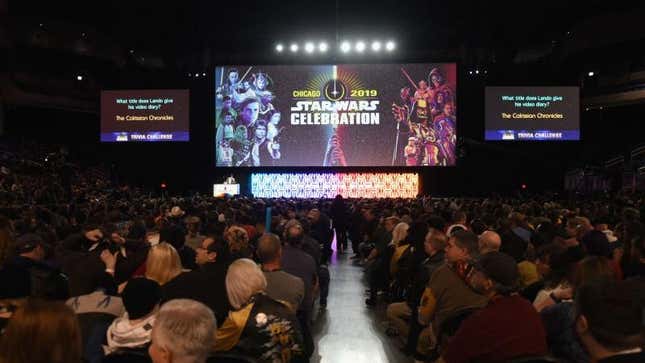 People sitting in a large room filled with large screens at Star Wars Celebration 2019.