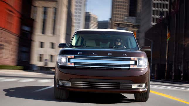 A photo of the front of a Ford Flex driving through a city. 