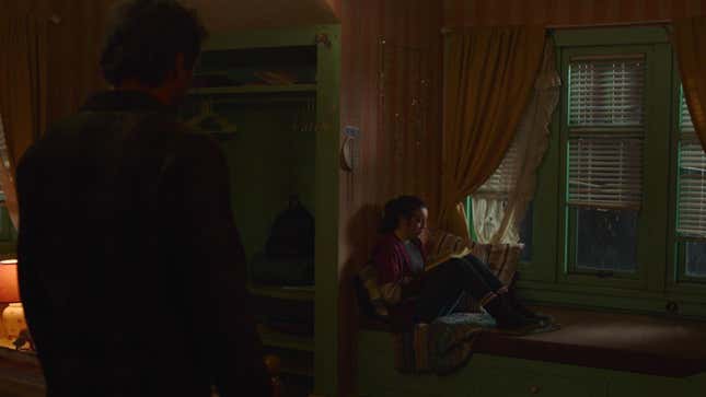 Ellie reads a book near a window as Joel faces her in a scene from HBO's The Last of Us.
