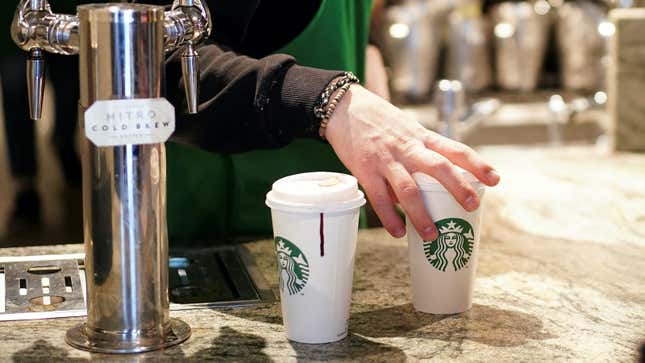 The hands of a Starbucks barista holding Starbucks single-use coffee cups