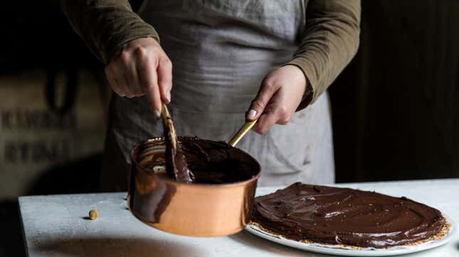  Two hands stirring a copper pot of melted chocolate being used to top a tart