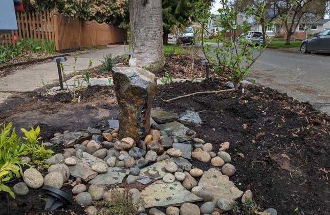 Image of a rock bubbler on a parking strip surrounded by rocks and plants.