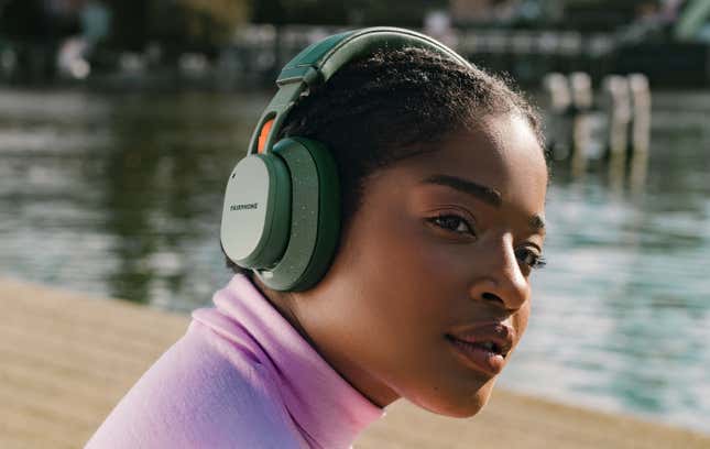 Una persona con la versión verde moteada de los auriculares inalámbricos Fairphone XL, sentada frente a una pequeña masa de agua.