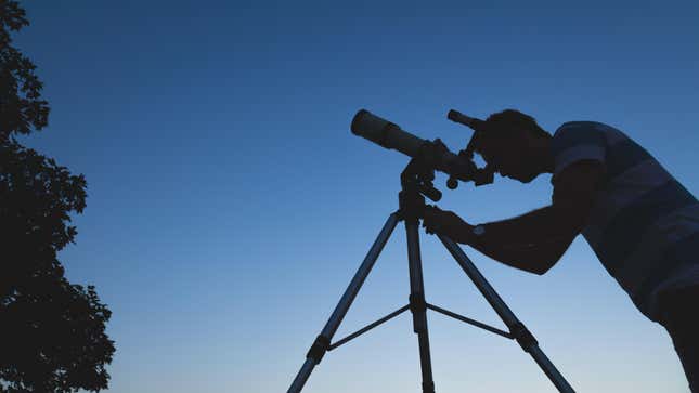 Man looking through telescope at dusk