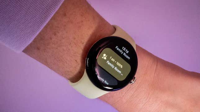 A Google Pixel Watch on a hand with a purple background and screen reading "Family Room"