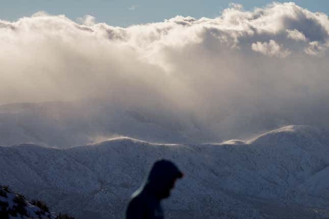 A visitor at a scenic outlook is backdropped by snow-covered mountains near Hesperia, California on Wednesday, March 1, 2023.