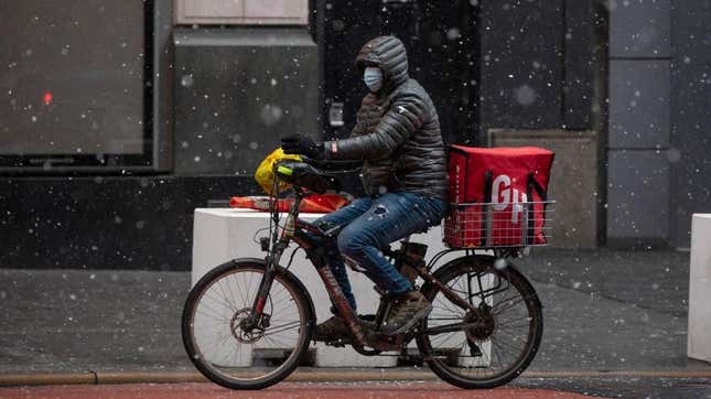 A Grubhub delivery driver carries food on a bike through the snow
