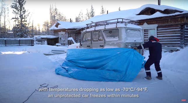 A man wraps a blue tarp around the base of an off-road vehicle to start it in extreme cold.