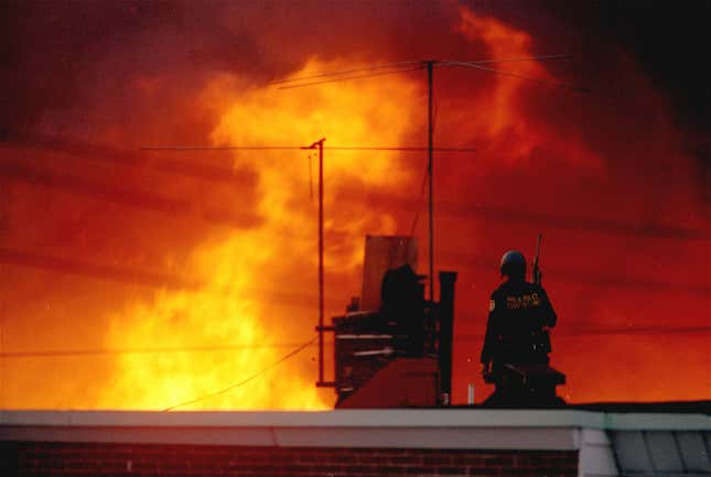 In this May, 1985 file photo, a Philadelphia policeman is seen on a rooftop as flames rise from a row of burning homes beyond, in Philadelphia. The fire started when police dropped a bomb onto the house of the militant group MOVE, on May 13, 1985 and fire spread throughout the area.